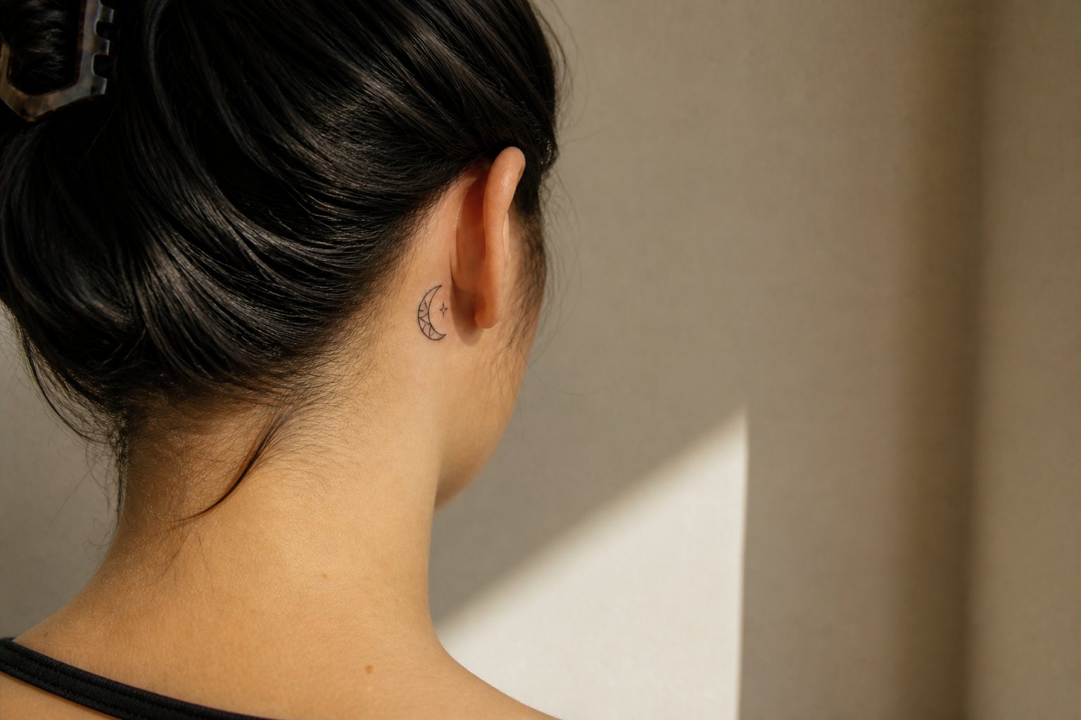A tiny stained-glass crescent and star tattoo behind an adult woman’s ear