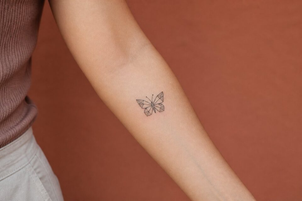 A small geometric butterfly tattoo on an adult woman’s forearm