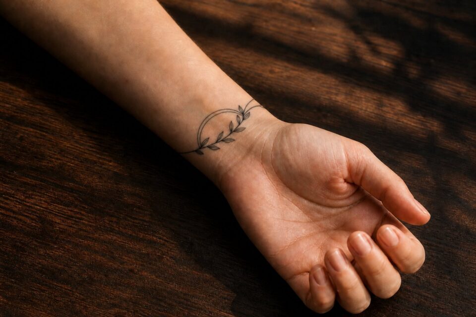 A small olive branch woven through an open wrist arc on an adult woman’s wrist