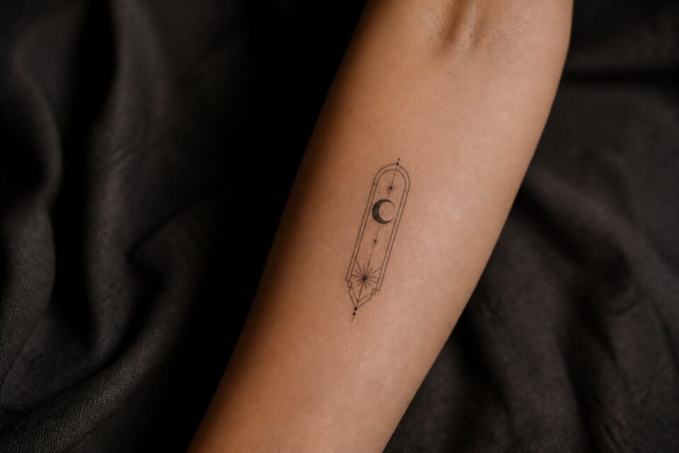 A small architectural moon and stars protection tattoo on an adult woman’s forearm